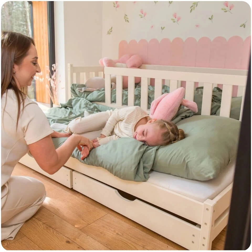 White COLA children's bunk bed with safety rail and pull-out drawer. A child is lying on green bedding.