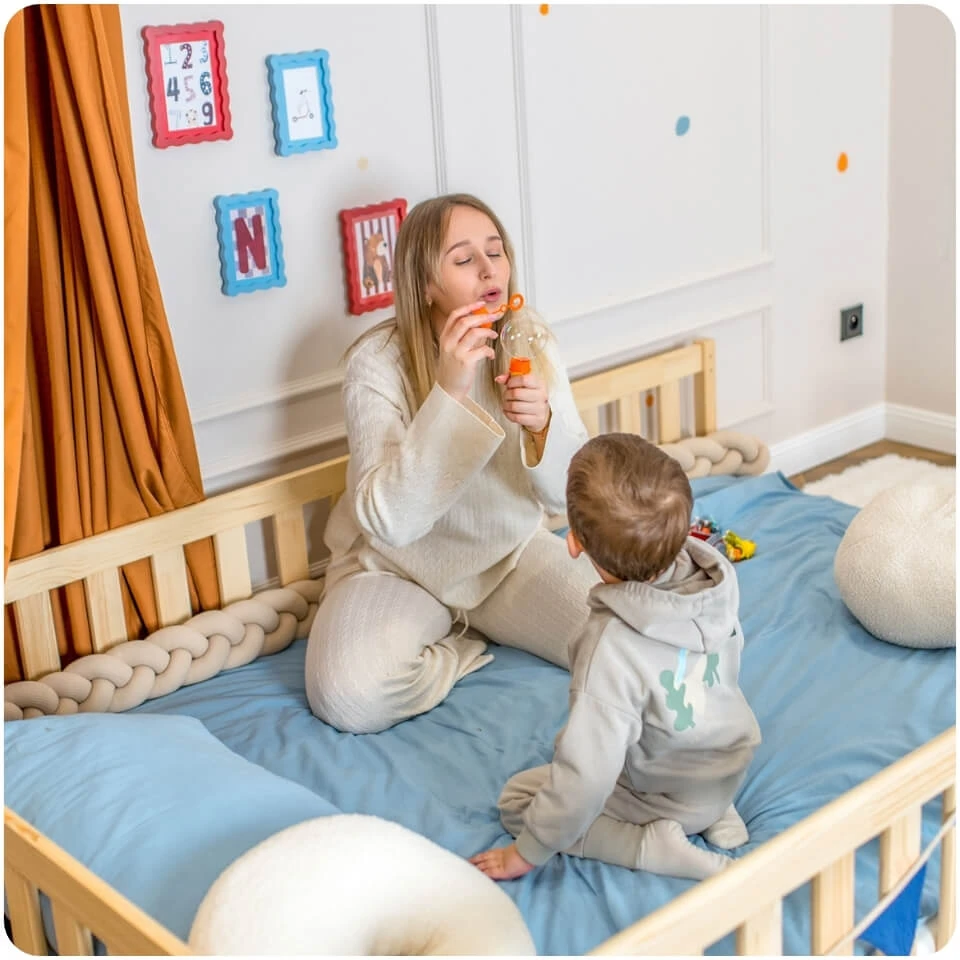 A mother and her son are sitting on a pine floor bed in a colourful room decorated with a circus theme.