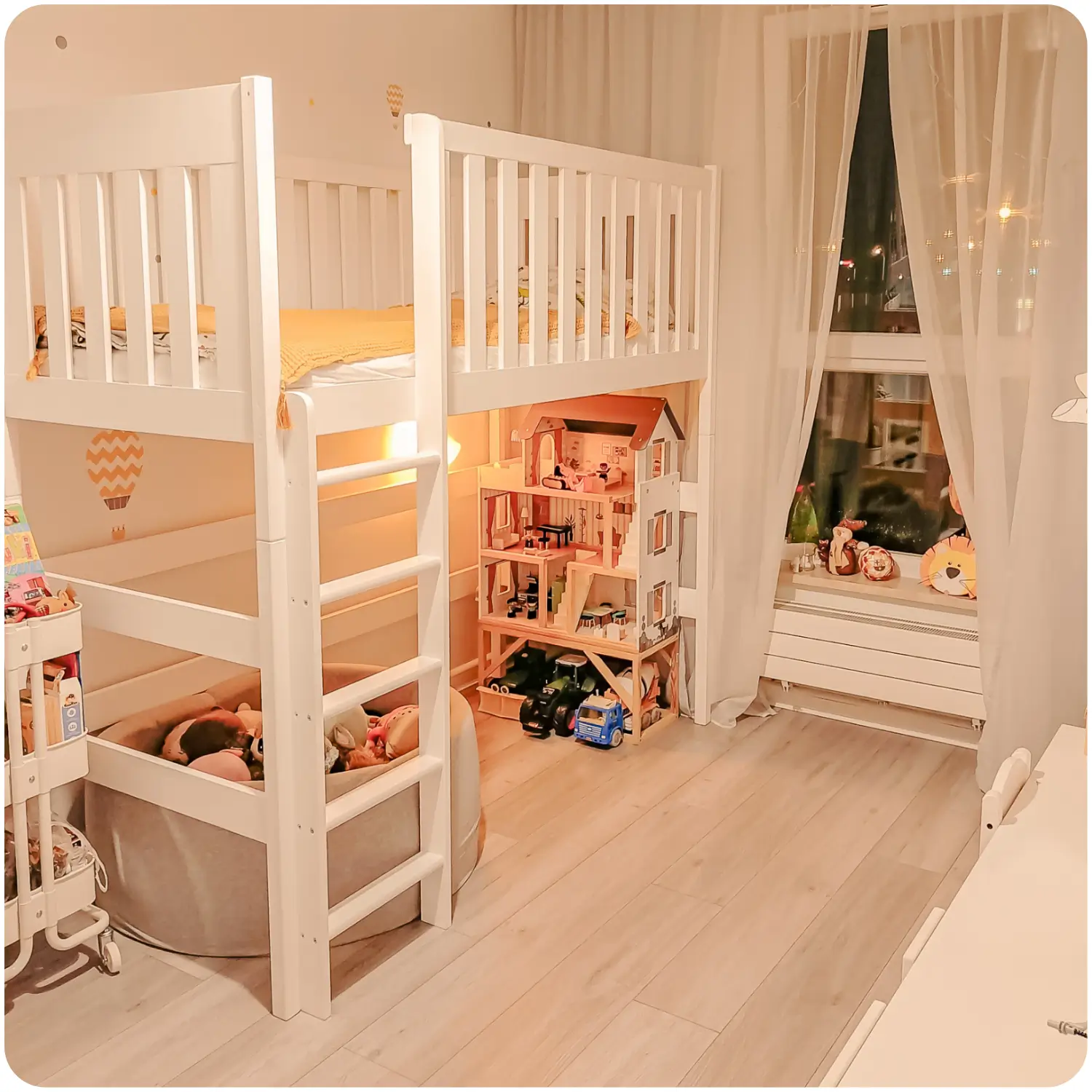 White children's loft bed LAURA with high railings. Under the bed is a play corner with a pool for stuffed animals and a large dollhouse.